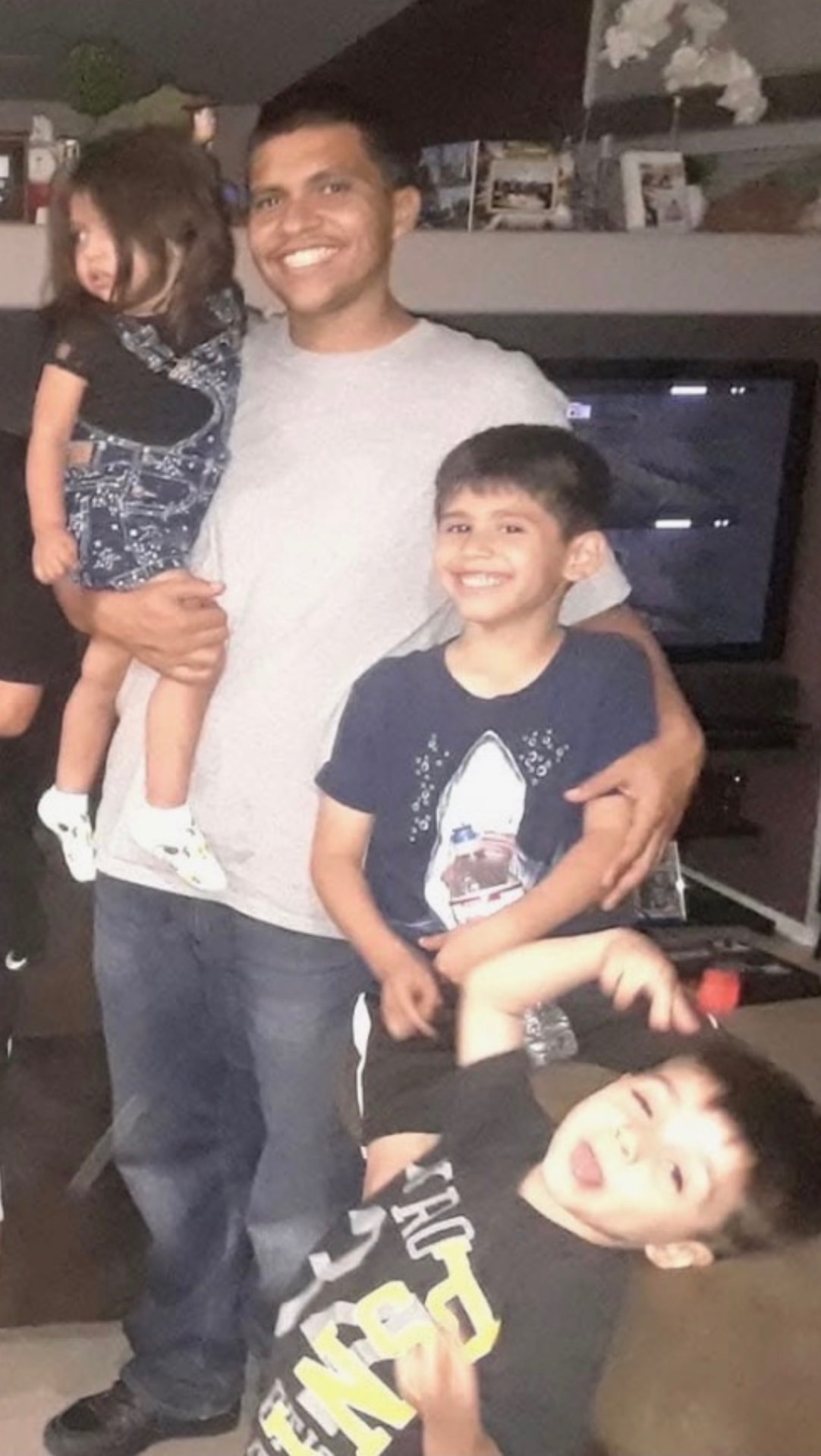 Mando holding a toddler girl with his arm around a boy while a younger boy hangs upside down