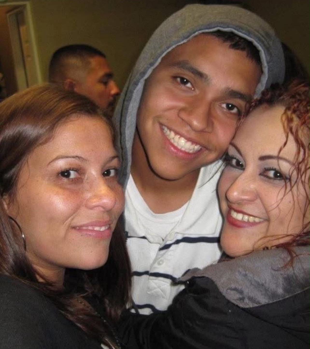 Mando in a gray hoodie smiling between two family members