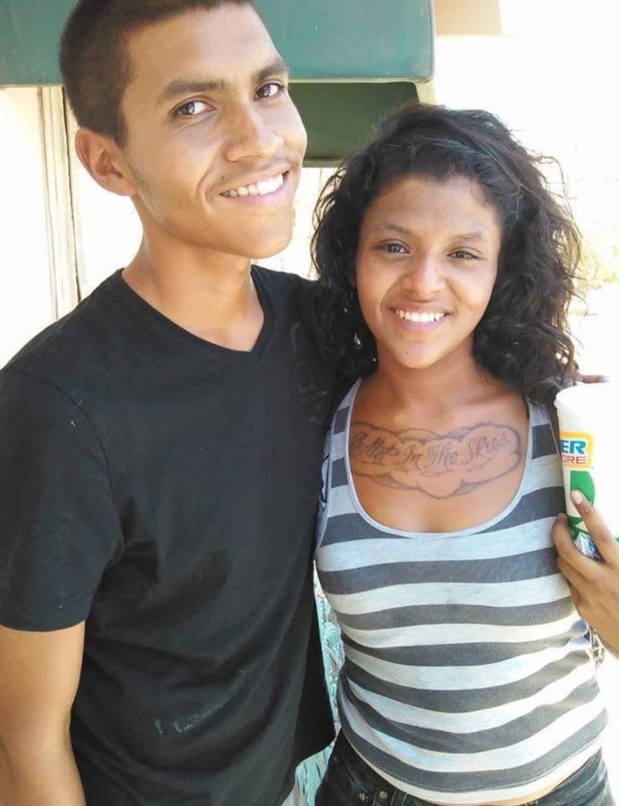 A young man and a woman standing close together outdoors with a drink