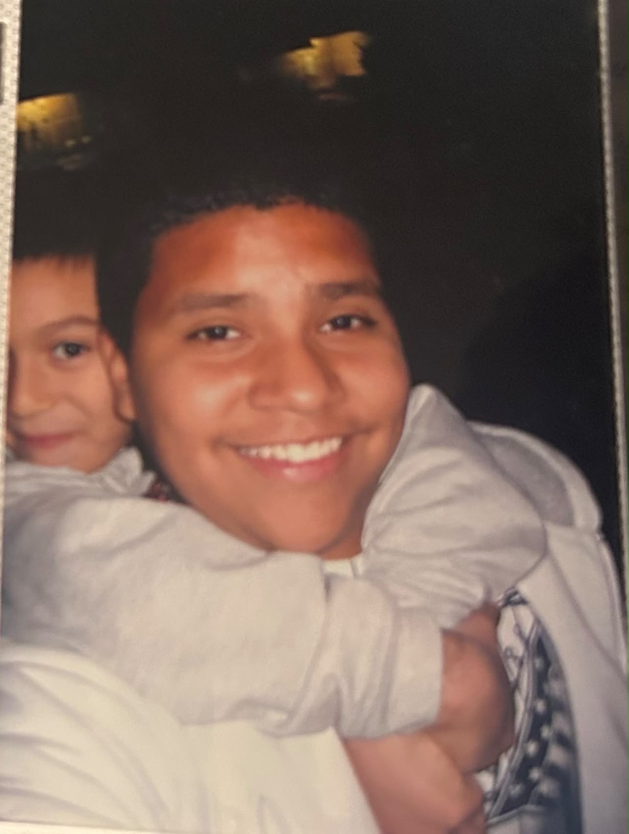 Young Mando smiling brightly with a friend peeking over his shoulder