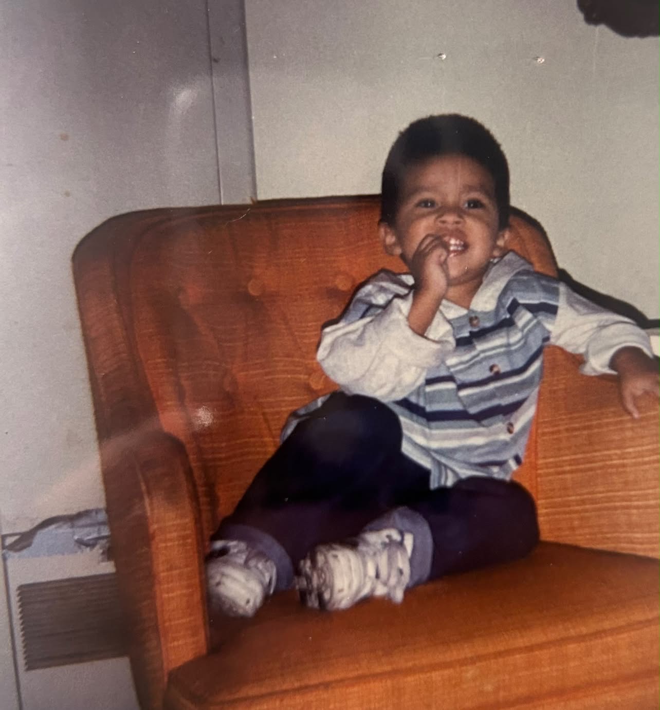Mando as a smiling toddler sitting in an orange armchair