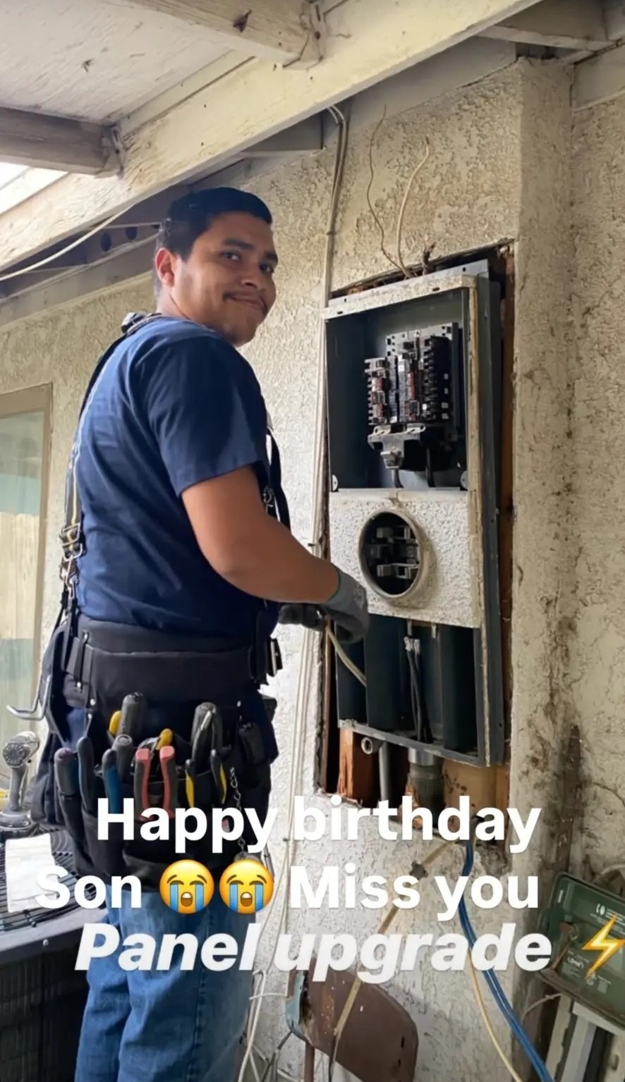 Mando in a tool belt smiling over his shoulder while working at an open electrical panel