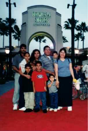 Mando as a boy in a red shirt standing with family at dusk