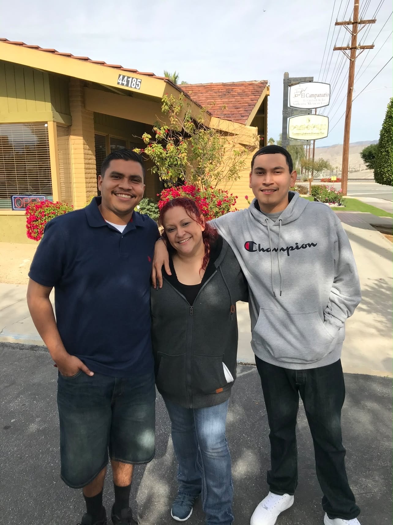 Mando in a navy polo shirt smiling outdoors between two family members