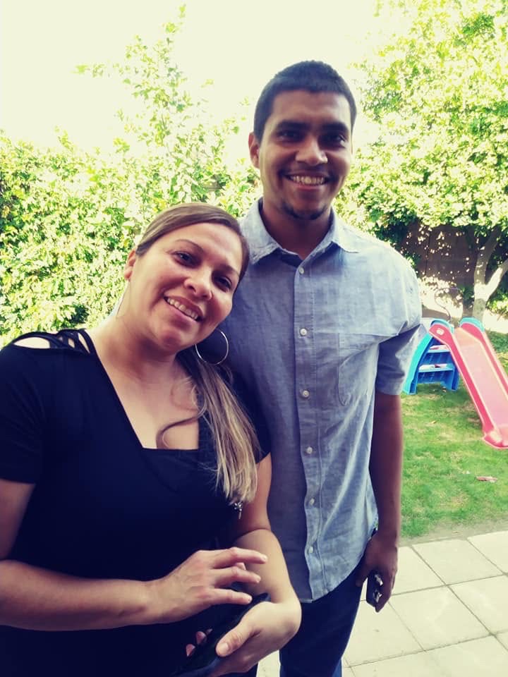 Mando in a light blue shirt standing close with a woman on a sunny patio