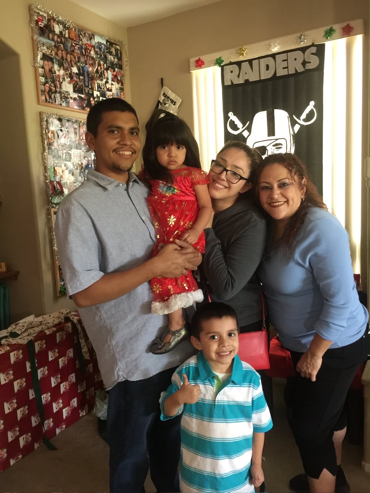 A family of five together in a living room decorated for Christmas, a Raiders flag in the window
