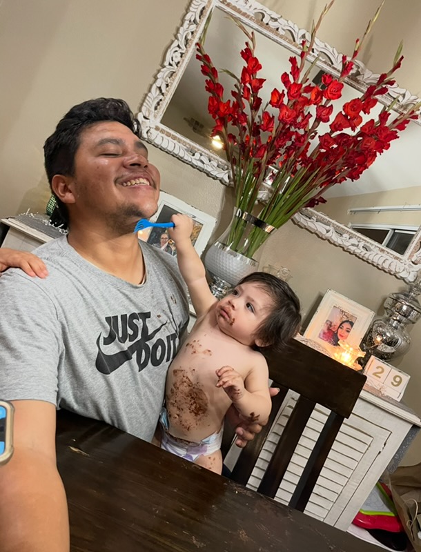 Mando laughing as a baby covered in cake frosting sits on his lap