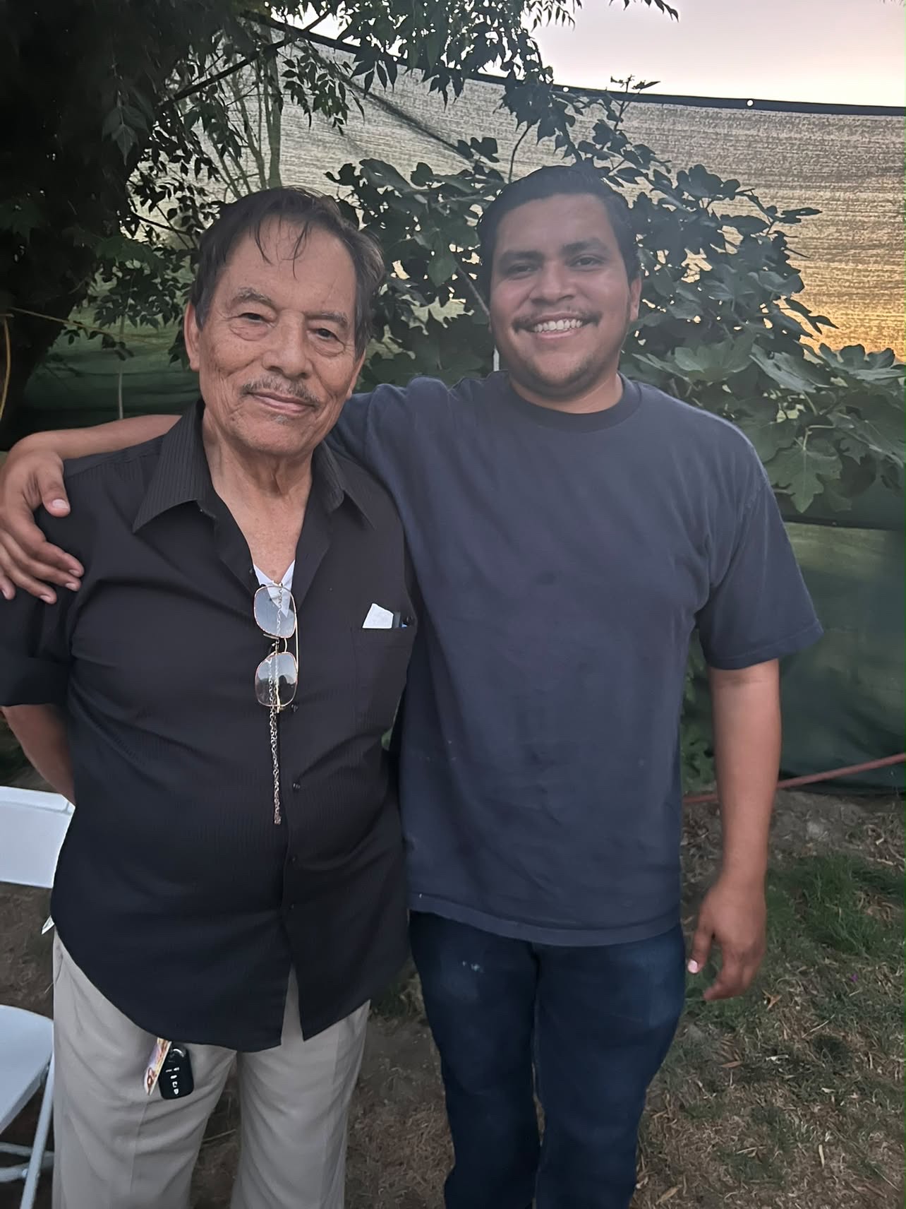 Mando with his arm around his grandfather in the backyard at sunset