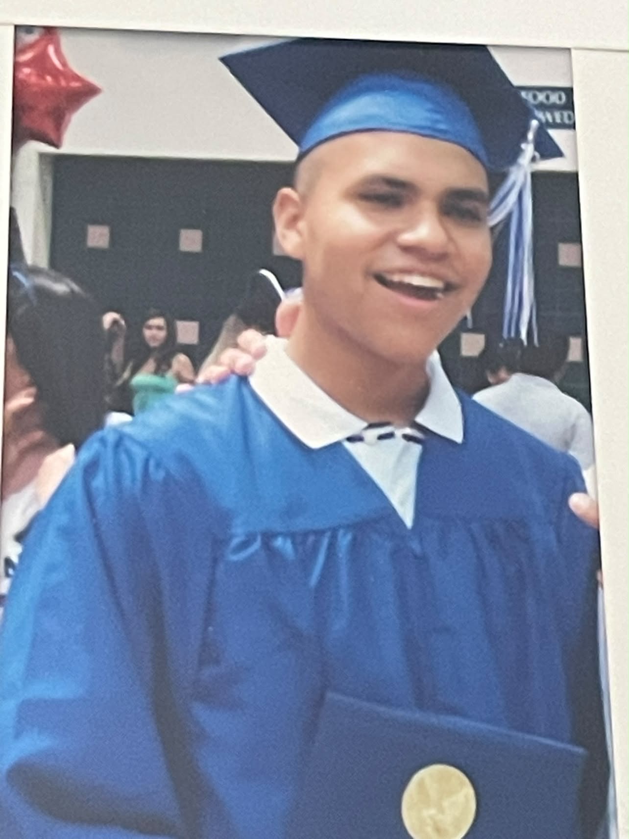 A young man in a blue graduation cap and gown holding his diploma