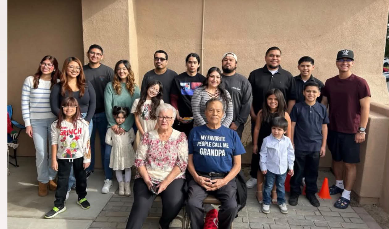 A large family gathered outdoors with an elderly couple seated in the center